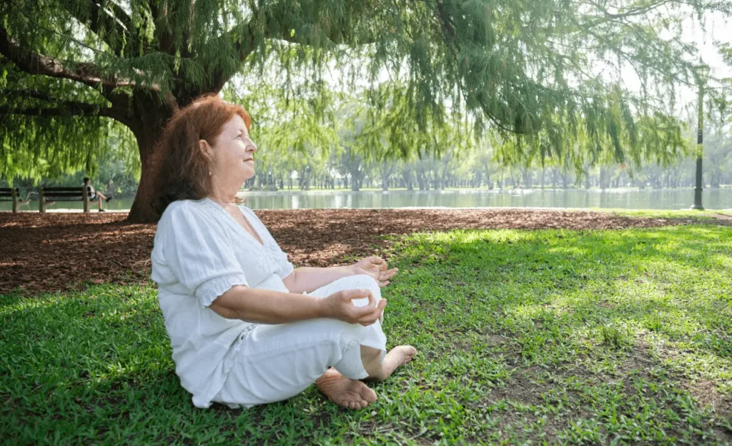 Older woman meditating outdoors to support overall wellness and bone health during osteoporosis treatment.